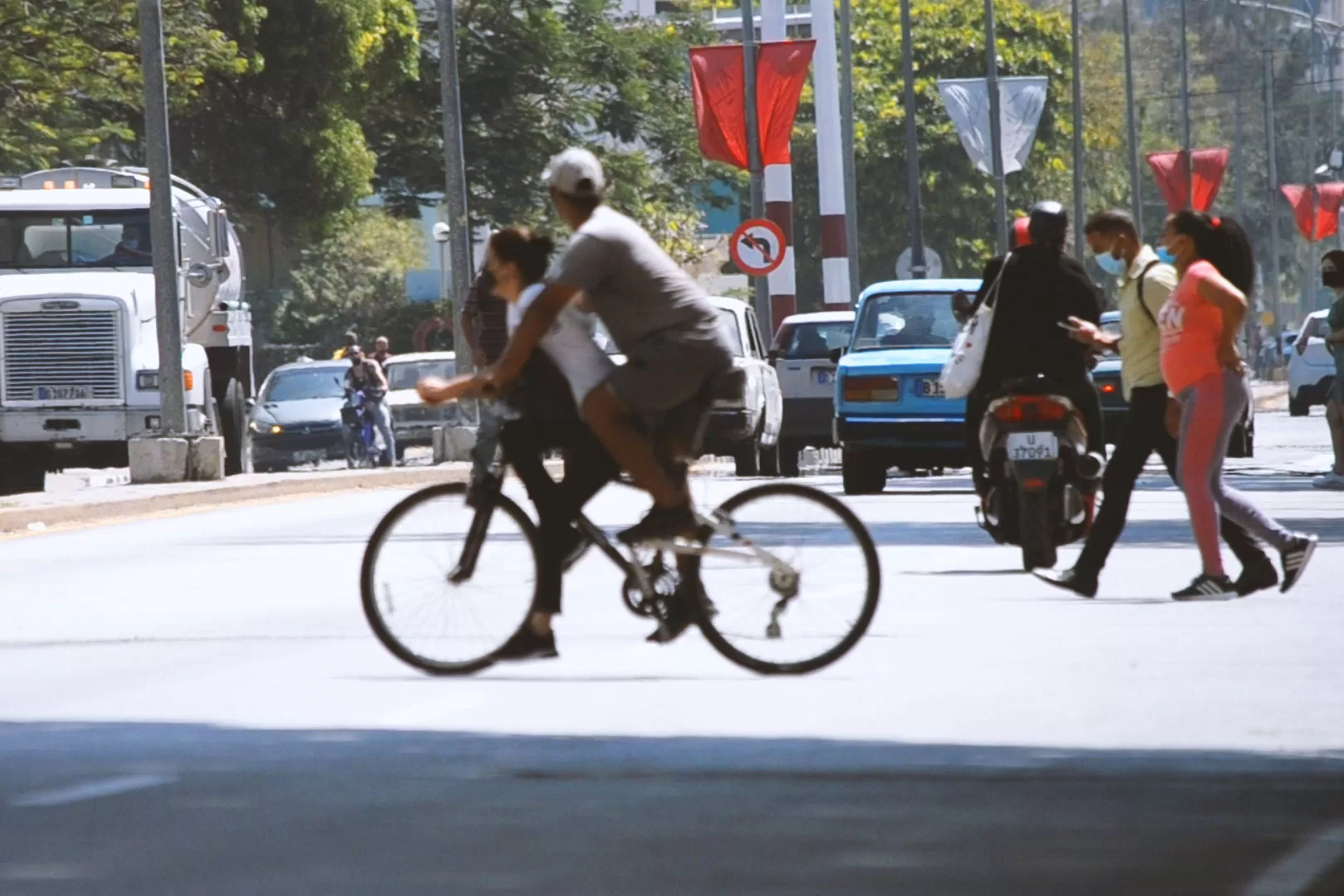 Dos ciclistas van en la misma bicicleta. La mujer está sentada en el cuadro de la bici.