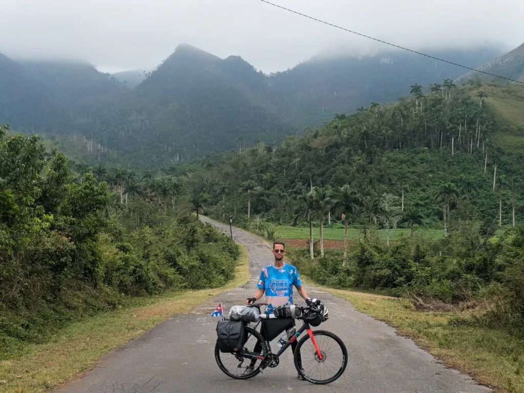 Pavel posa con su bicicleta y al fondo se ve una gran sierra de montañas